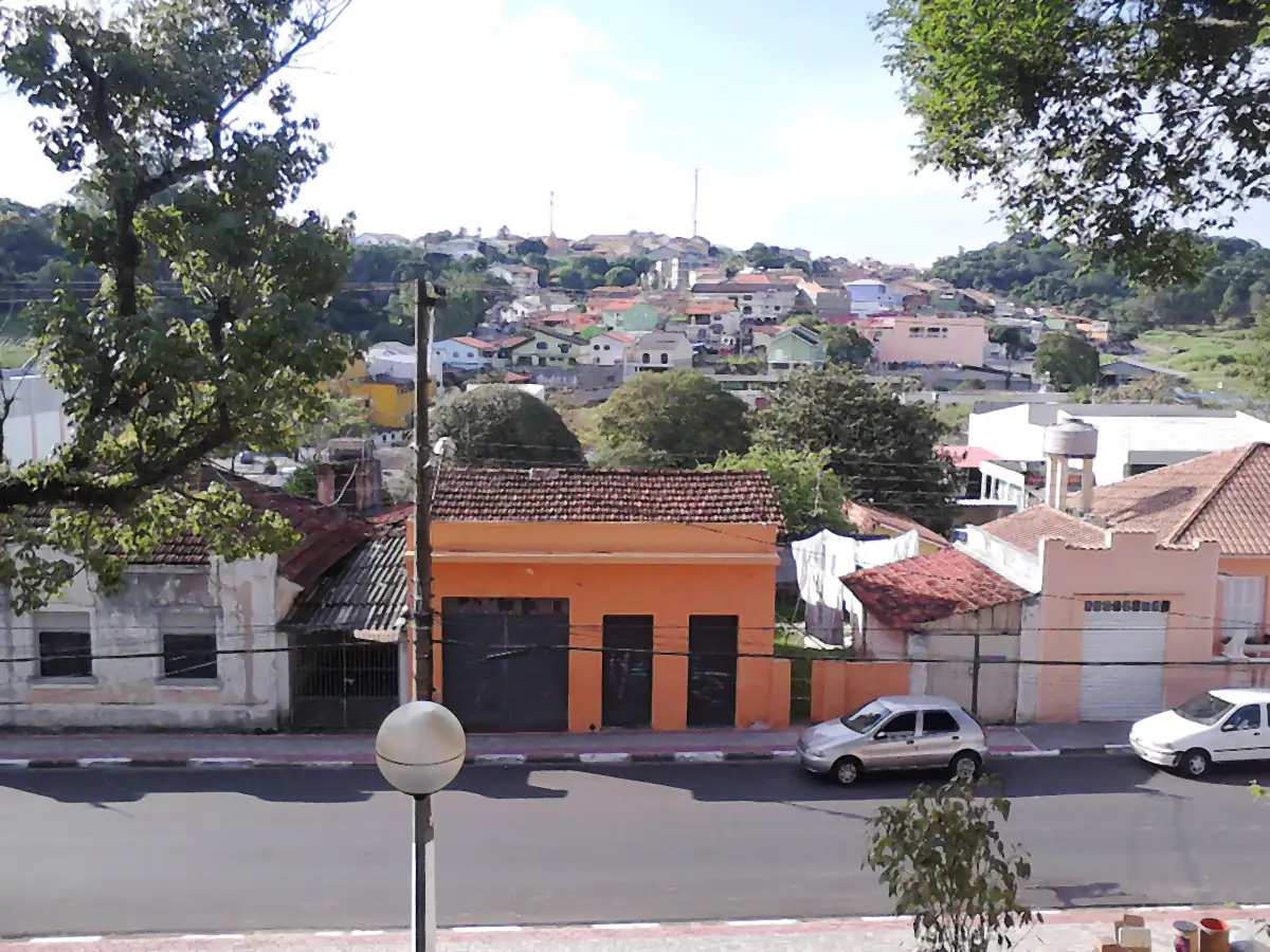 Vista de Arujá a partir da Praça da Matriz, com casas no morro e céu parcialmente nublado