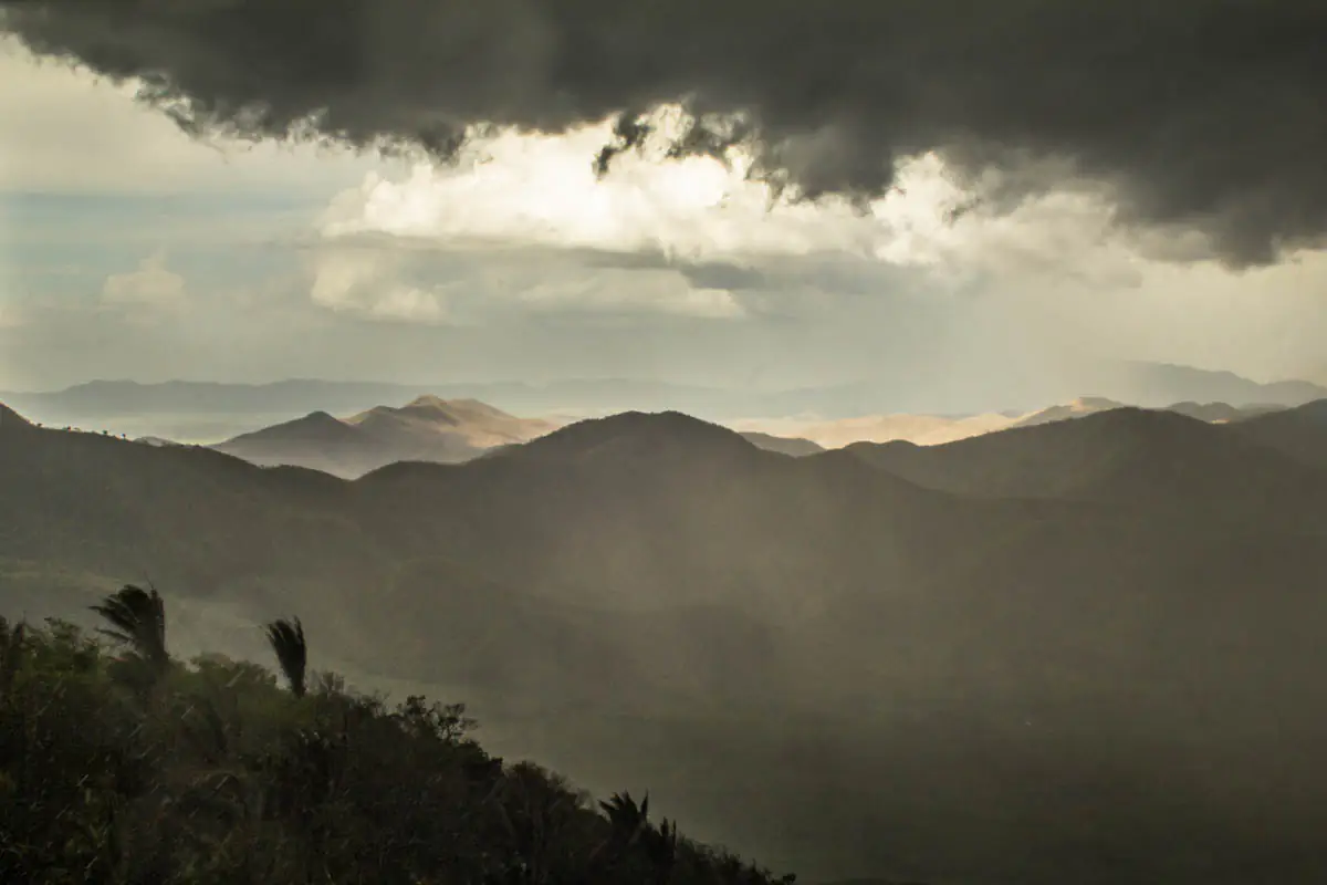 Chuva caindo sobre morros da Serra da Ibiapaba, sob nuvem escura e com luz do sol ao fundo