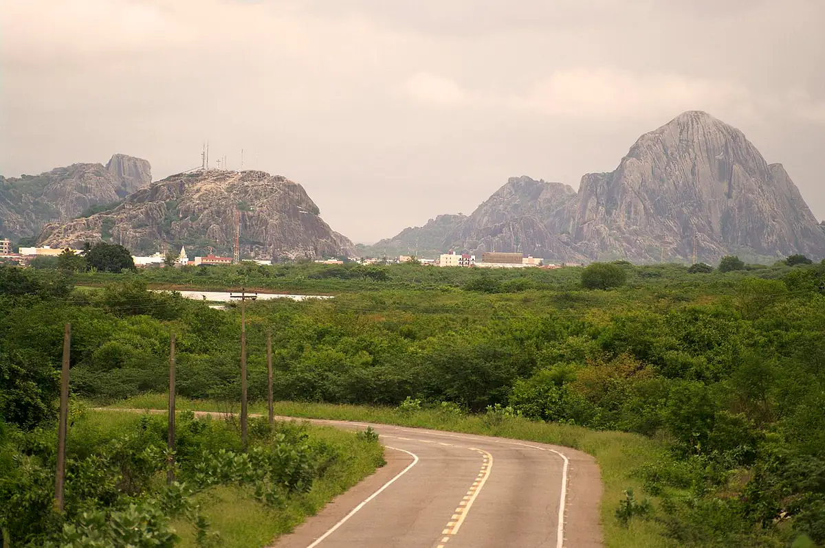Estrada no Sertão Central cercada de caatinga verde, com monólitos de granito e céu nublado ao fundo