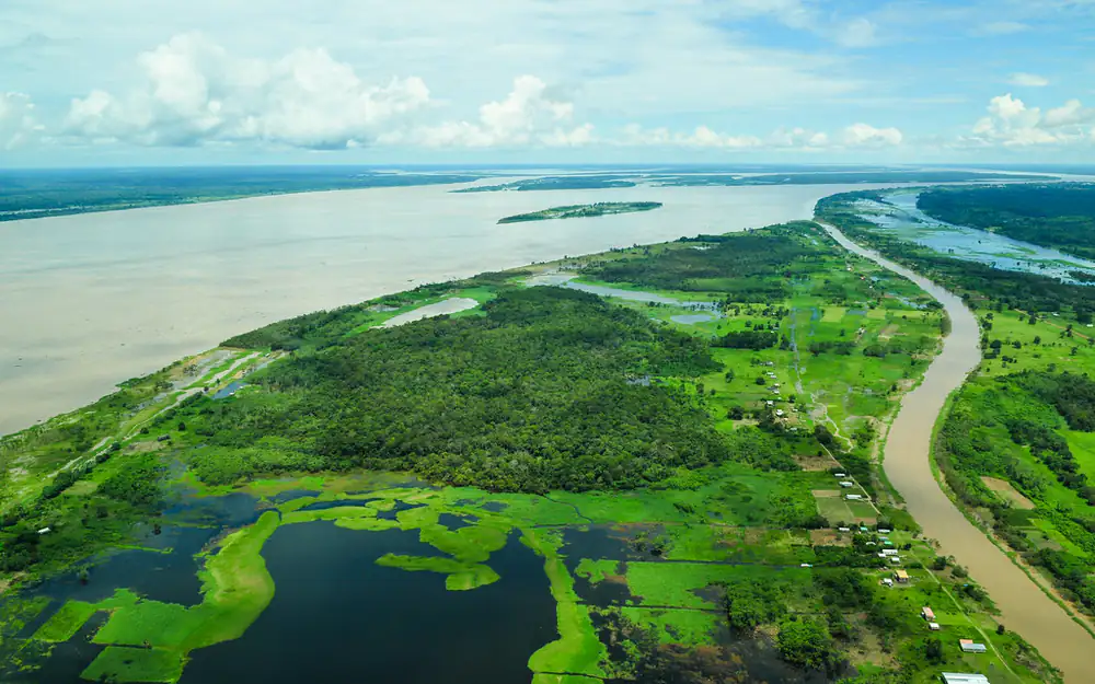 Vista aérea da Floresta Amazônica com rio largo, lagos e mata alagada sob céu com nuvens