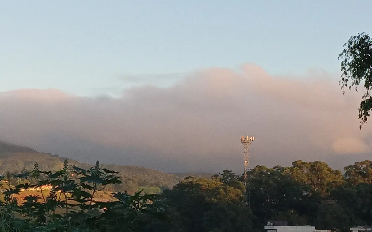 Grande nuvem escura de chuva se aproximando de morros e casas de Guarulhos no fim da tarde