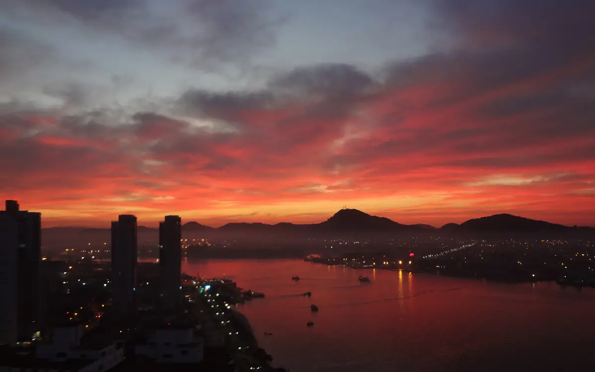 Céu alaranjado ao amanhecer sobre o mar e a entrada do porto na Ponta da Praia, em Santos