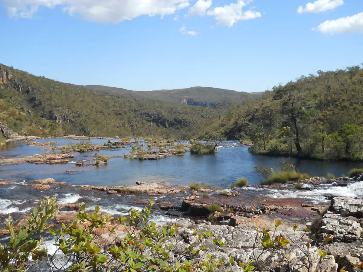 Rio com corredeiras entre morros cobertos de vegetação de Cerrado, sob céu azul