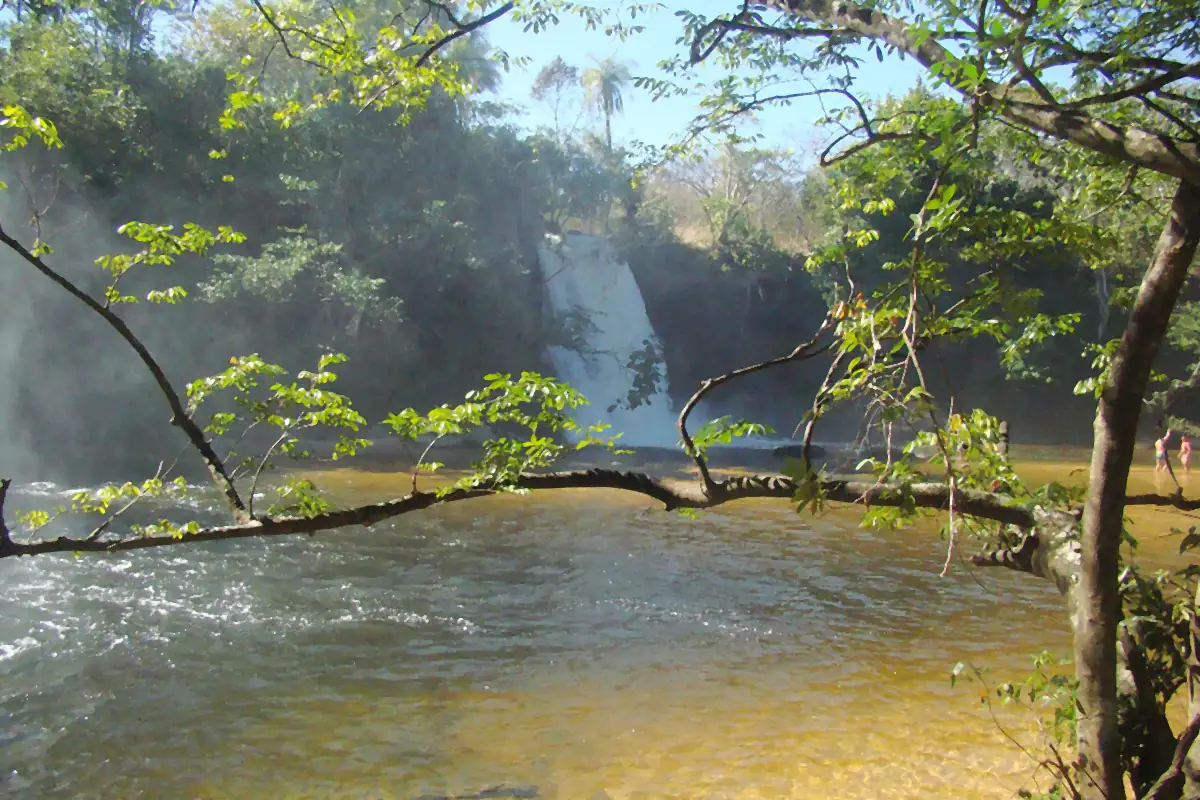 Cachoeira entre árvores do cerrado e rio de água amarelada no Parque Nacional da Chapada das Mesas