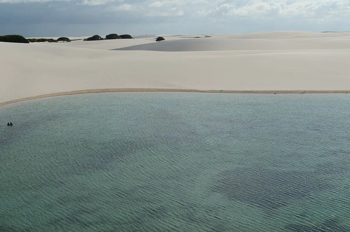 Lagoa cheia entre dunas brancas nos Lençóis Maranhenses, sob céu de nuvens