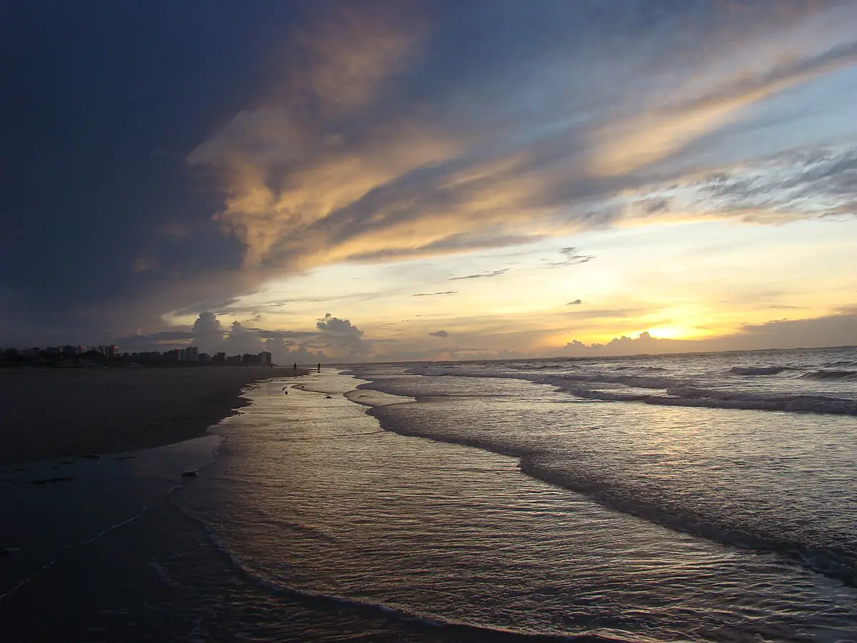 Praia do Calhau, em São Luís, ao entardecer, com nuvem de chuva escura sobre os prédios e ondas na areia molhada