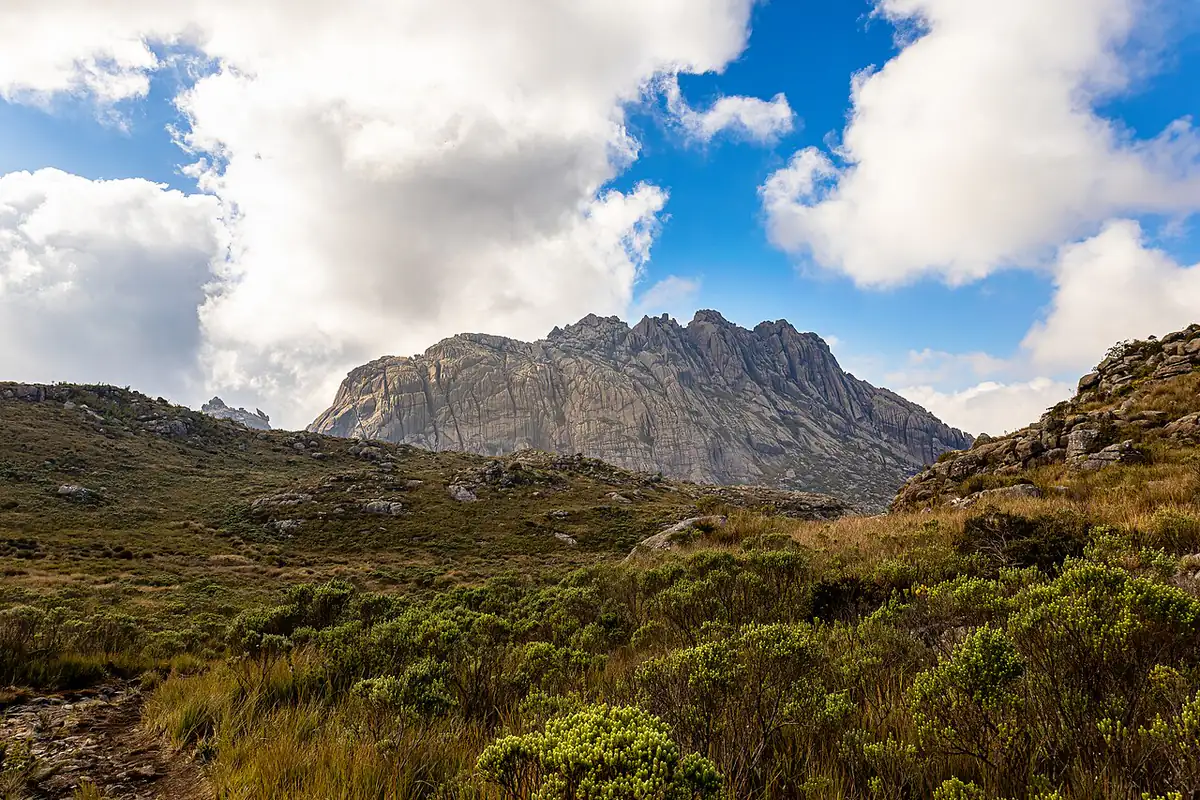 Paredão de pedra na parte alta do Parque Nacional do Itatiaia, com vegetação de altitude e nuvens no céu