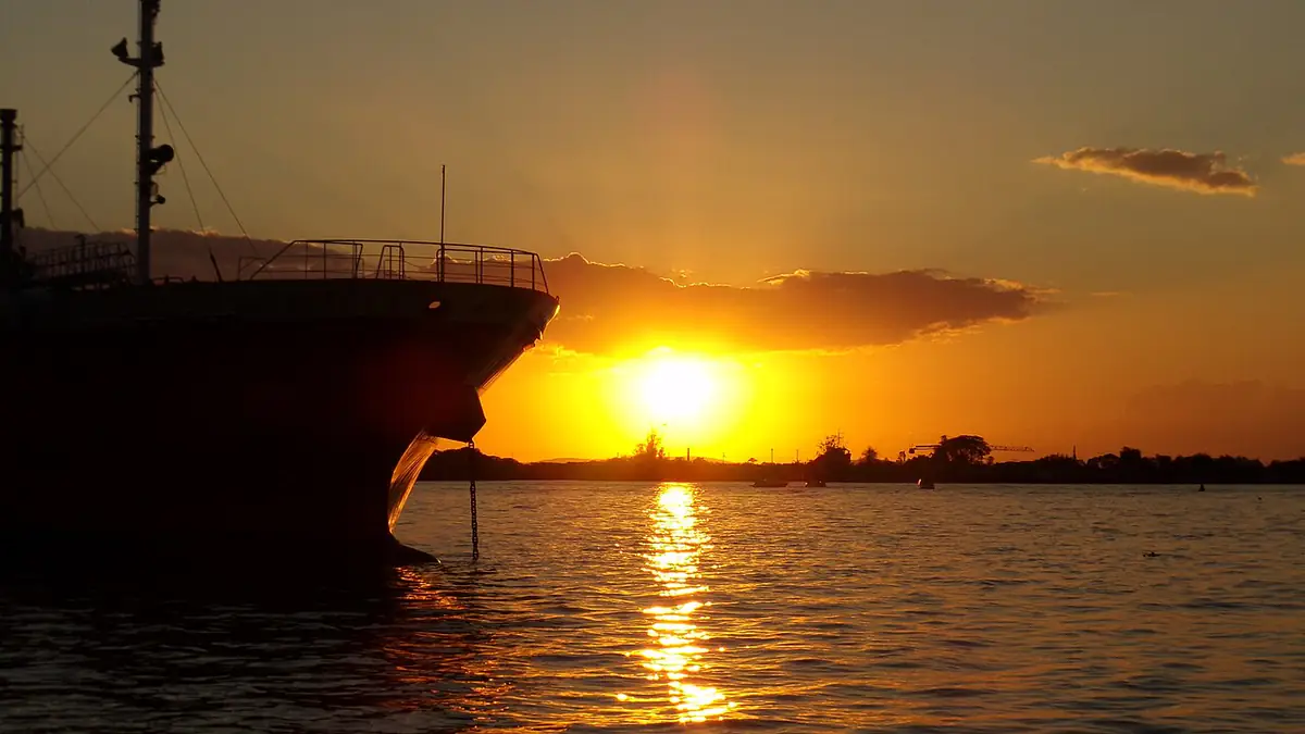 Pôr do sol alaranjado sobre o Lago Guaíba, com a proa de um navio em silhueta à esquerda