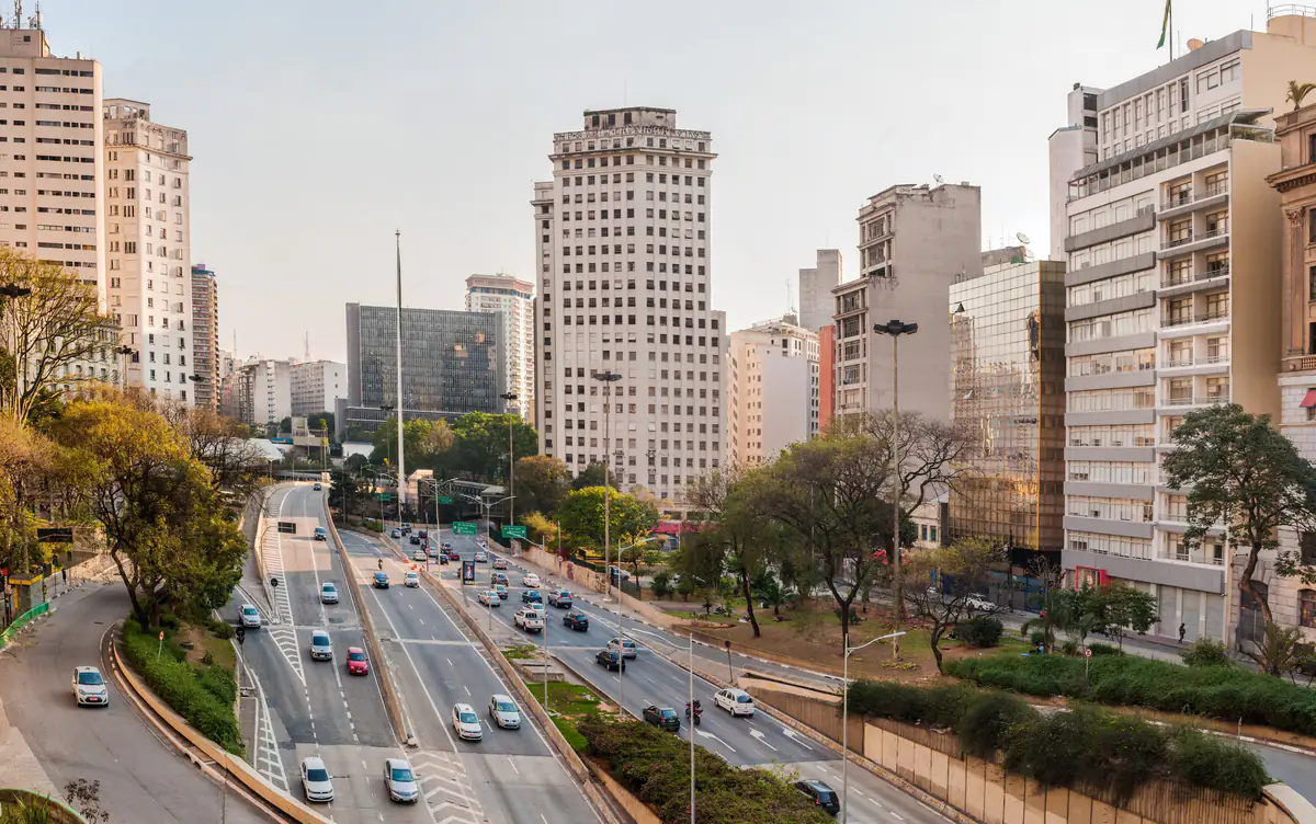 Avenida de várias pistas chegando ao centro de São Paulo, com prédios altos e céu seco e enevoado