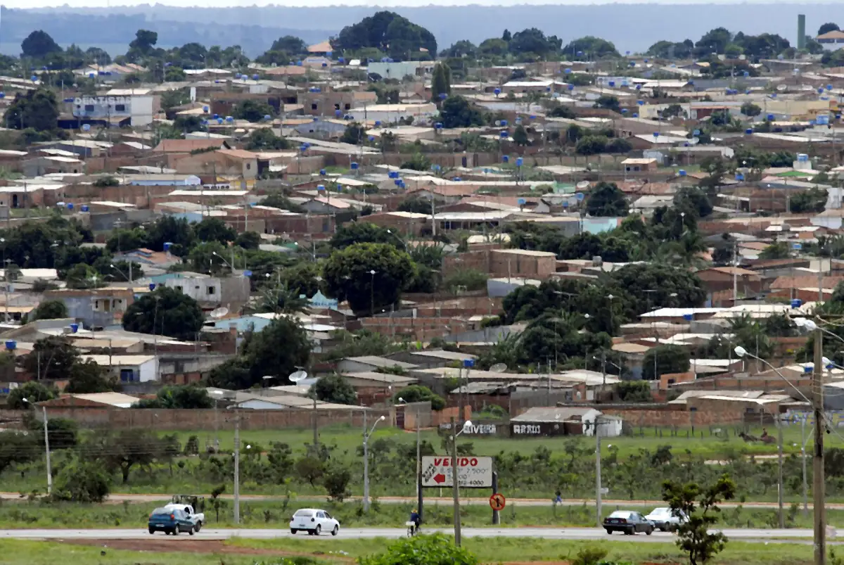 Casas e ruas de Águas Lindas de Goiás vistas de longe, com árvores, cerrado ao fundo e céu encoberto