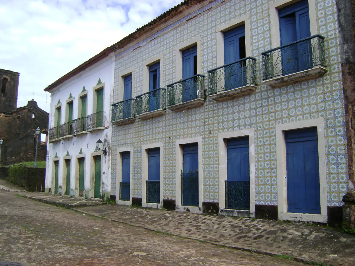 Casarões históricos revestidos de azulejos numa rua de pedra em Alcântara, com céu nublado ao fundo