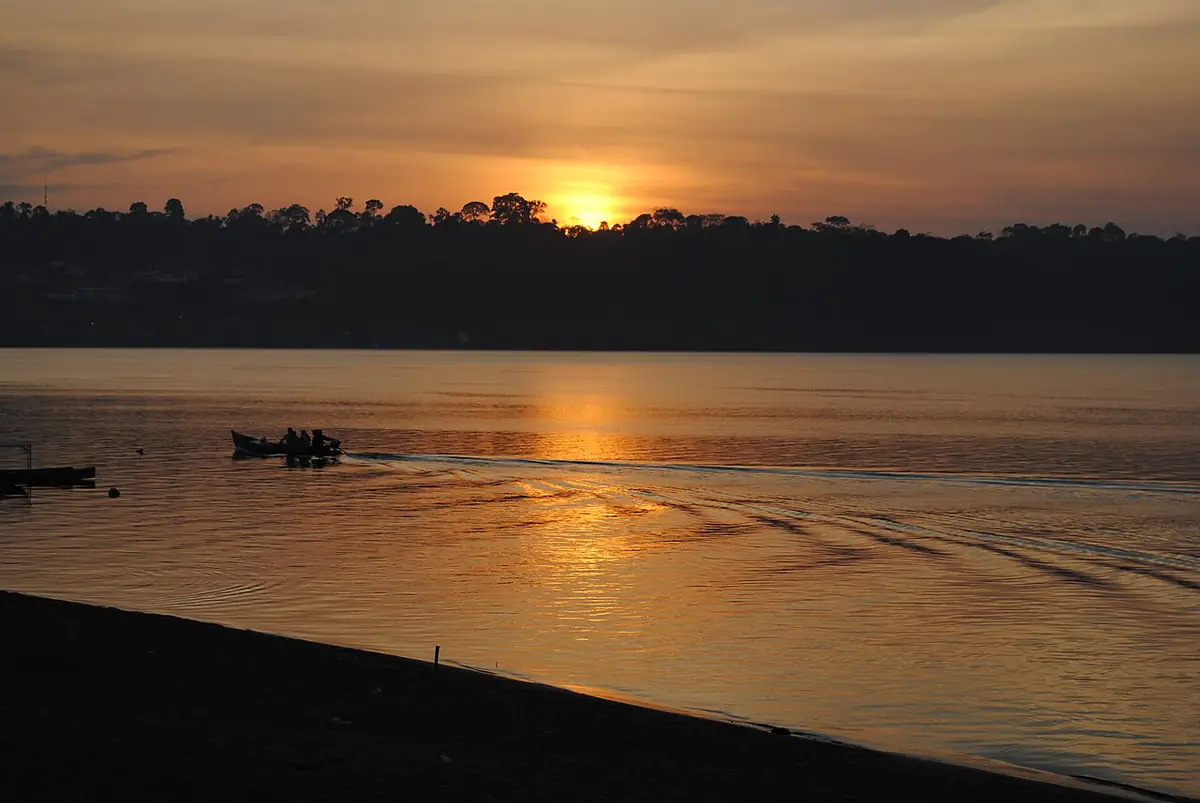 Nascer do sol sobre o Rio Xingu, com mata na outra margem e um barco com pessoas na água