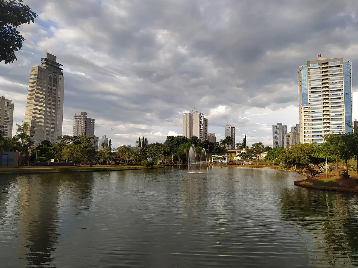 Lago do Parque Ambiental Ipiranga em Anápolis, com prédios do bairro Jundiaí ao fundo e céu carregado de nuvens