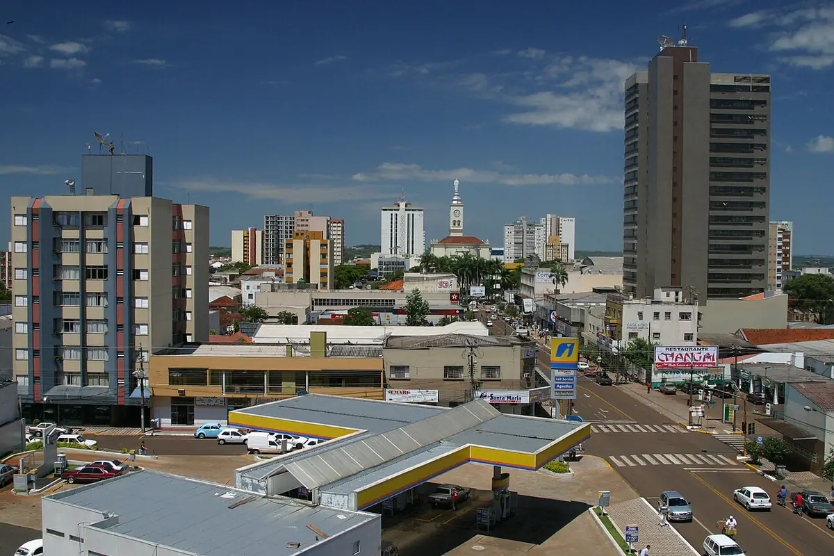 Centro de Apucarana visto do alto, com prédios, a torre do relógio da igreja e céu azul com poucas nuvens