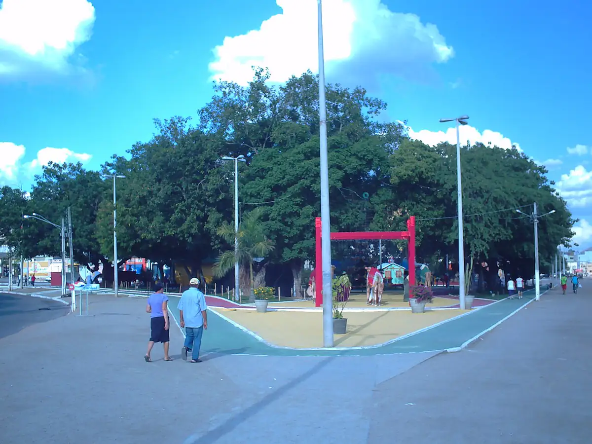 Praça Winston Siqueira, em Arcoverde, com árvores grandes e céu azul com nuvens