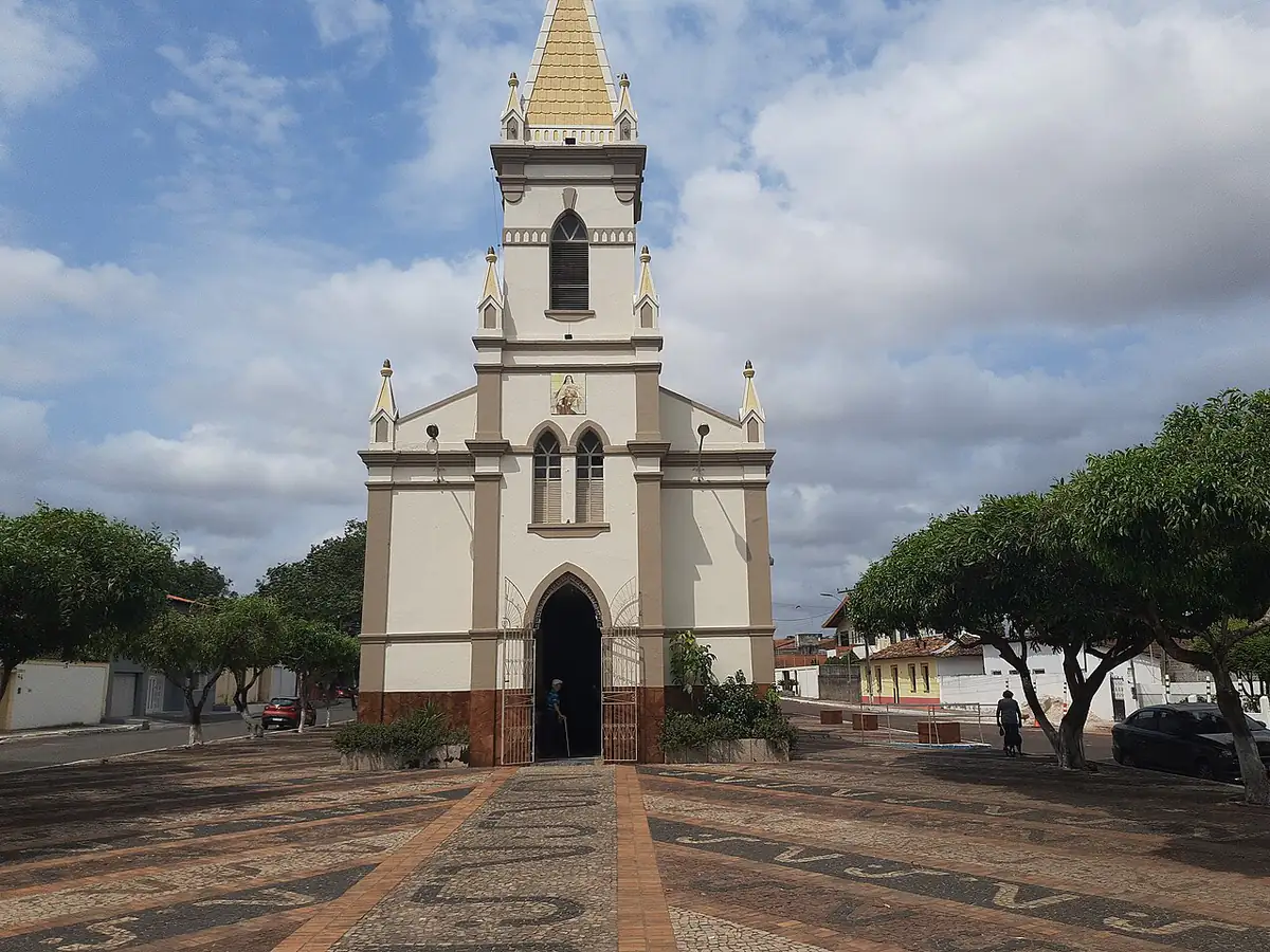 Catedral de Santa Teresinha, em Bacabal, com praça de pedra, árvores e céu com grandes nuvens