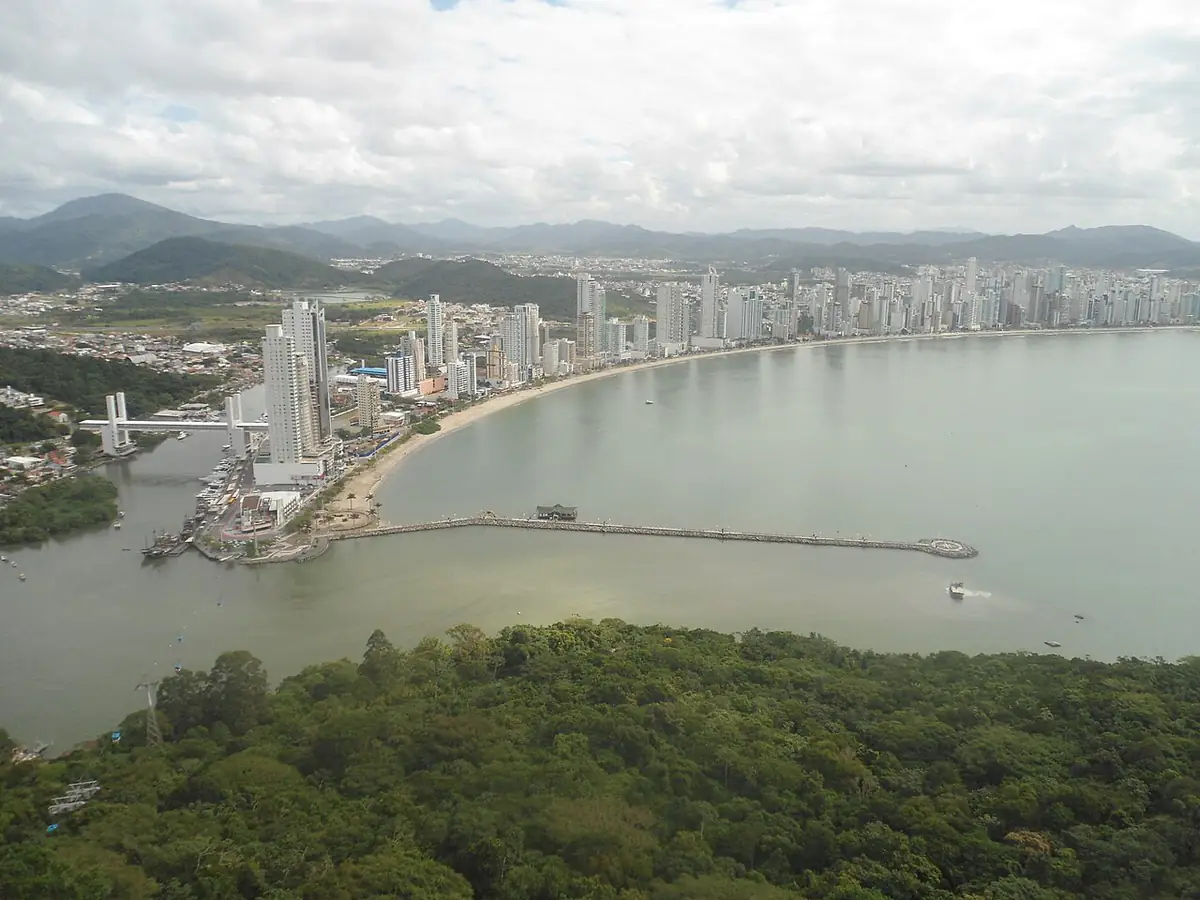 Vista do mirante do Parque Unipraias sobre a orla de Balneário Camboriú, com prédios altos, a baía calma e o céu nublado