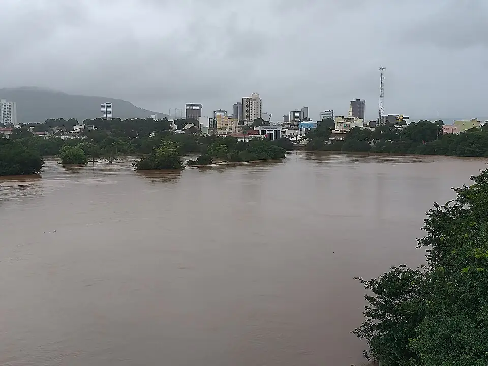 Rio Grande cheio e barrento diante dos prédios de Barreiras, sob céu cinzento de chuva