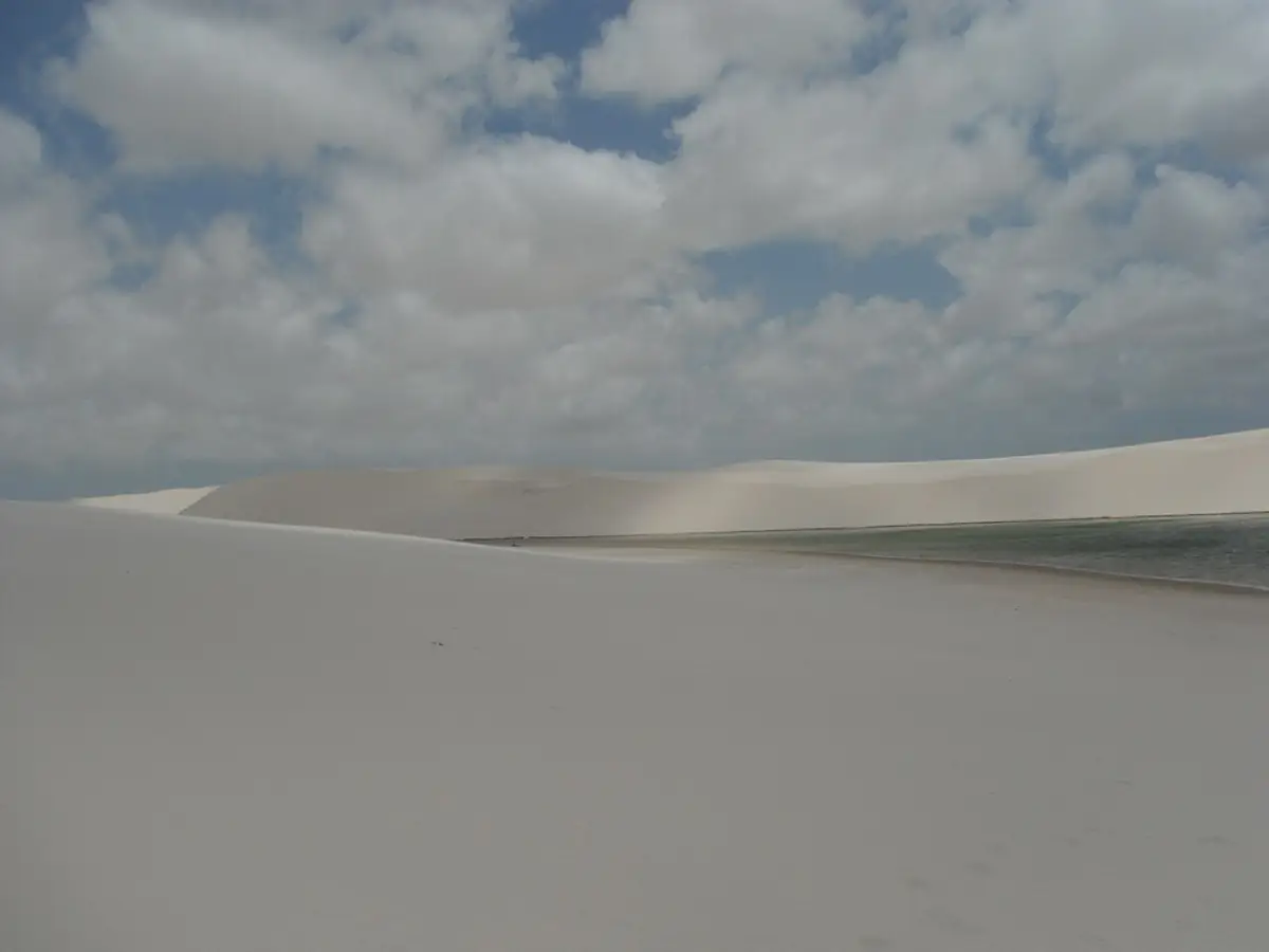 Dunas de areia branca e uma lagoa ao fundo, sob céu azul com muitas nuvens, nos Lençóis Maranhenses em Barreirinhas