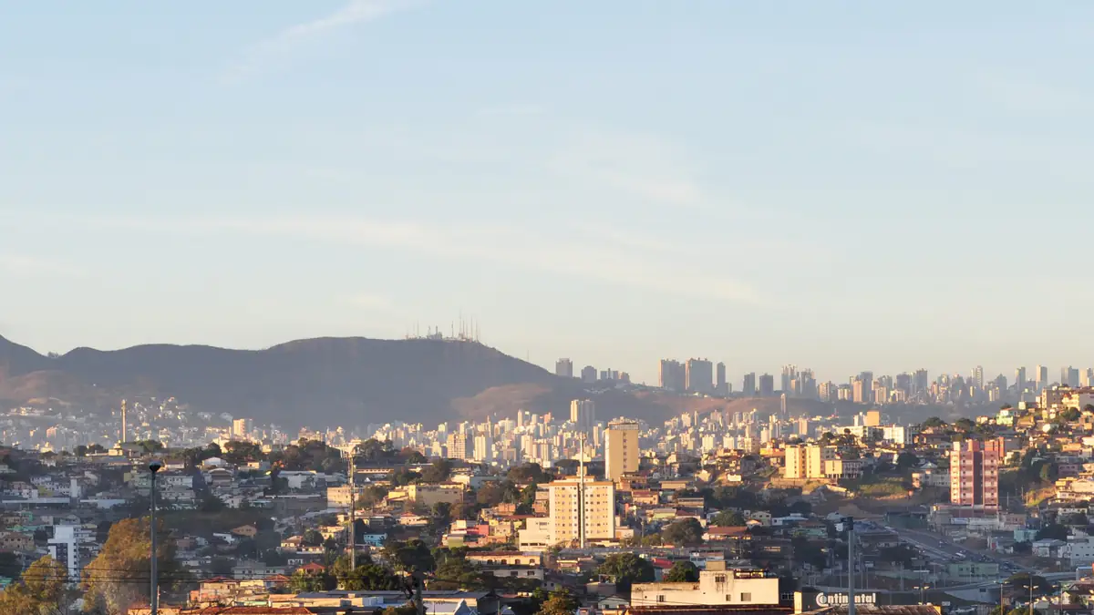 Prédios de Belo Horizonte vistos de longe, com a Serra do Curral ao fundo sob céu claro de manhã