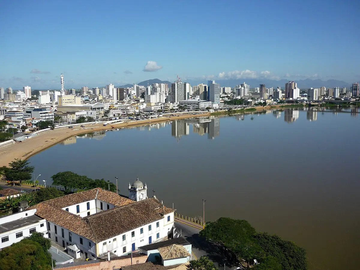Vista do centro de Campos dos Goytacazes, com prédios à beira do Rio Paraíba do Sul e serra ao fundo