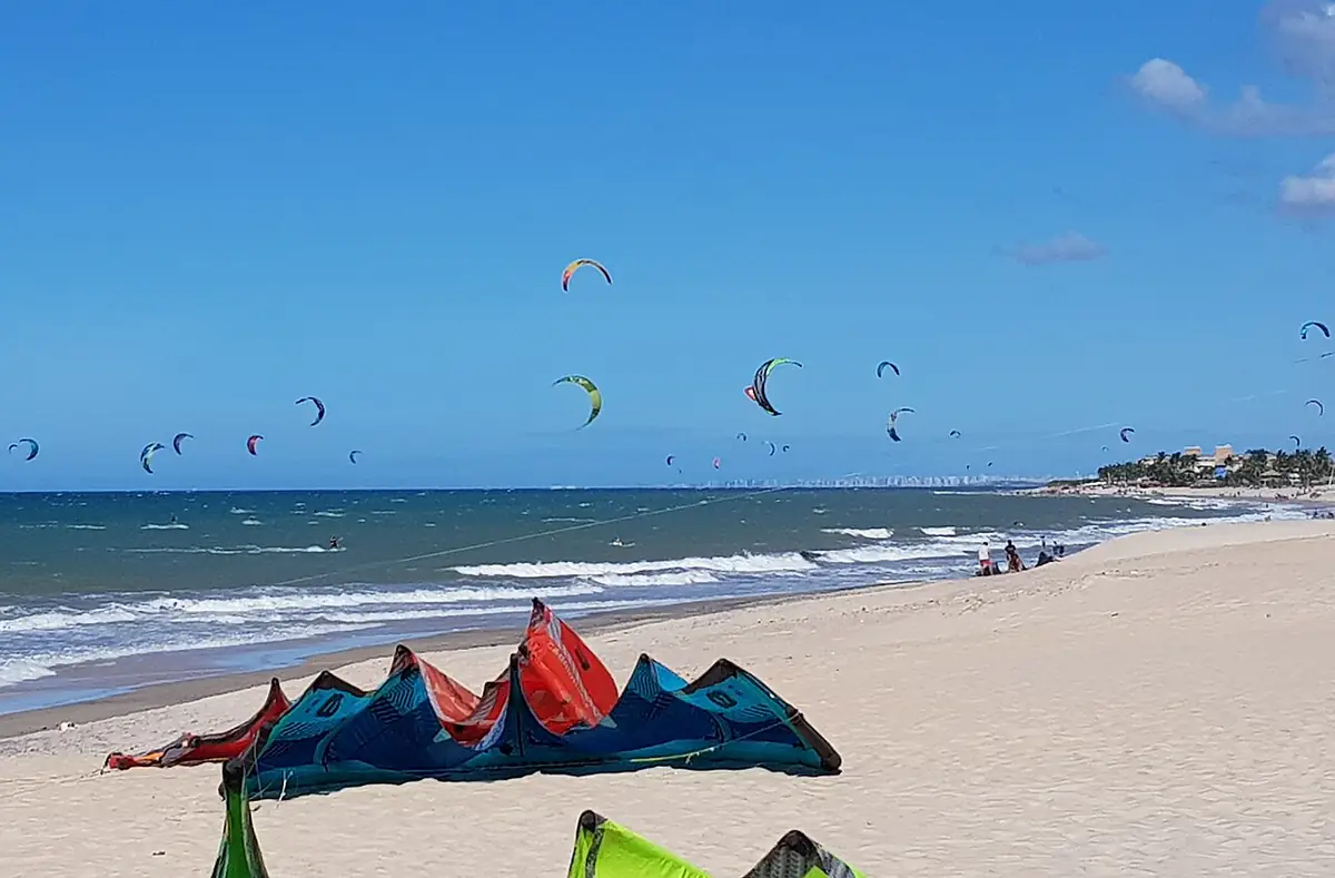 Pipas de kitesurf no céu azul sobre o mar e a areia da Praia do Cumbuco, em Caucaia