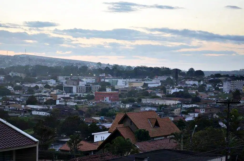 Vista parcial de Garanhuns ao entardecer, com telhados, árvores e colinas sob céu com nuvens