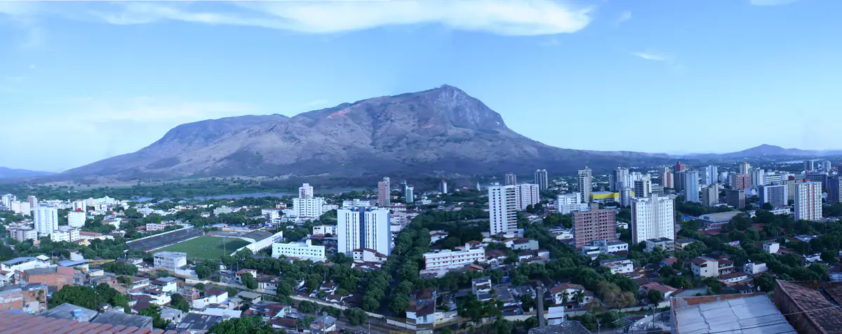 Vista panorâmica de Governador Valadares com o Pico da Ibituruna ao fundo, sob céu azul com poucas nuvens