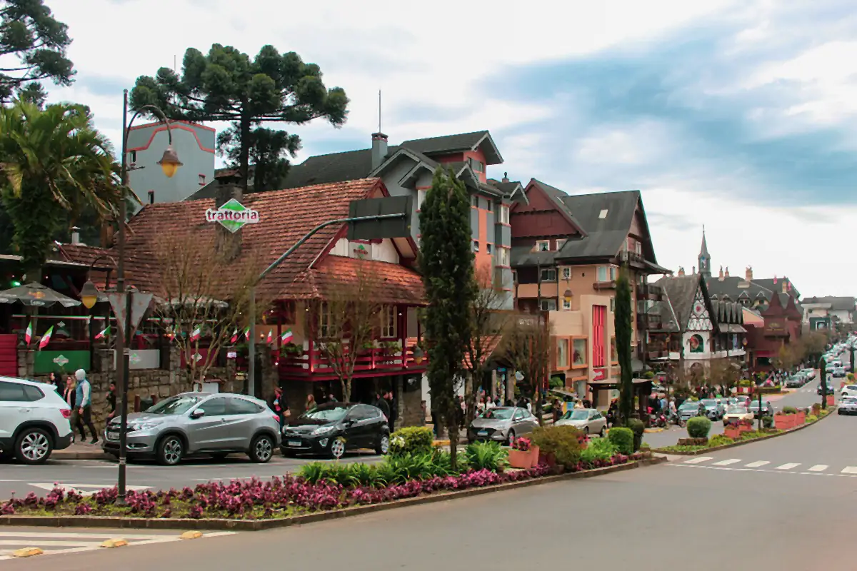 Rua do centro de Gramado com casas de telhado inclinado, araucárias e céu nublado em dia de inverno