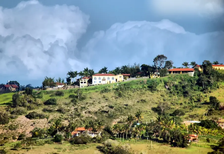 Casas em uma encosta verde de Gravatá, com grandes nuvens carregadas no céu