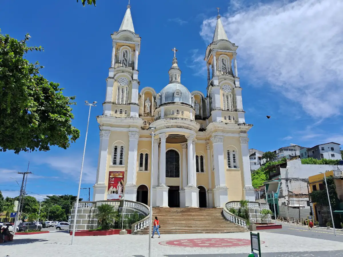 Catedral de São Sebastião, em Ilhéus, com duas torres e cúpula, sob céu azul com nuvens