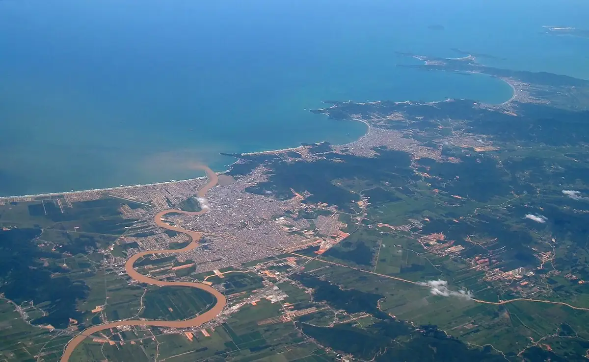 Vista aérea de Itajaí na foz do rio Itajaí-Açu, com o rio marrom em curvas desaguando no mar azul e a cidade junto à costa