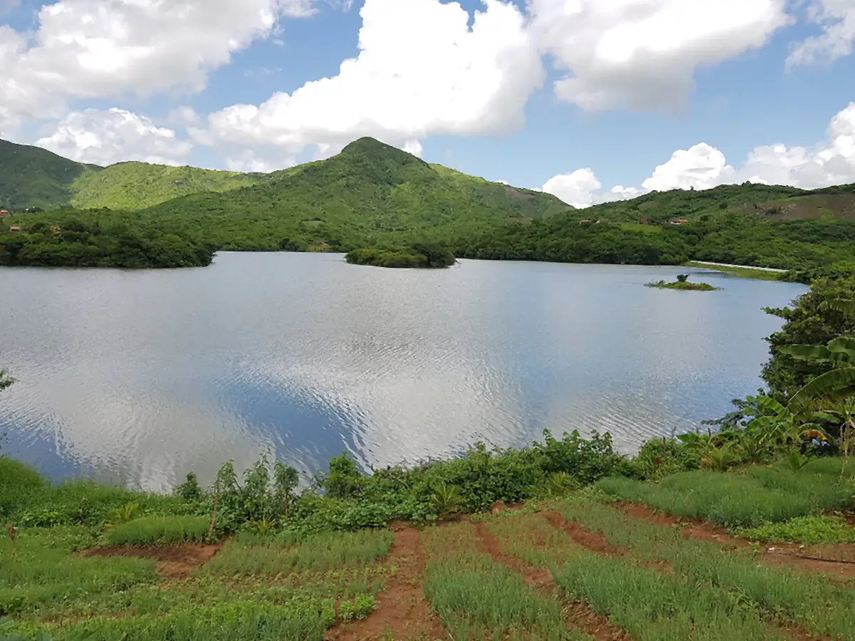 Açude Quandu, em Itapipoca, cercado por morros verdes sob céu azul com nuvens carregadas