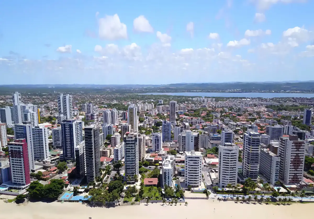 Vista aérea de Candeias, em Jaboatão dos Guararapes, com prédios junto à praia e céu azul com nuvens