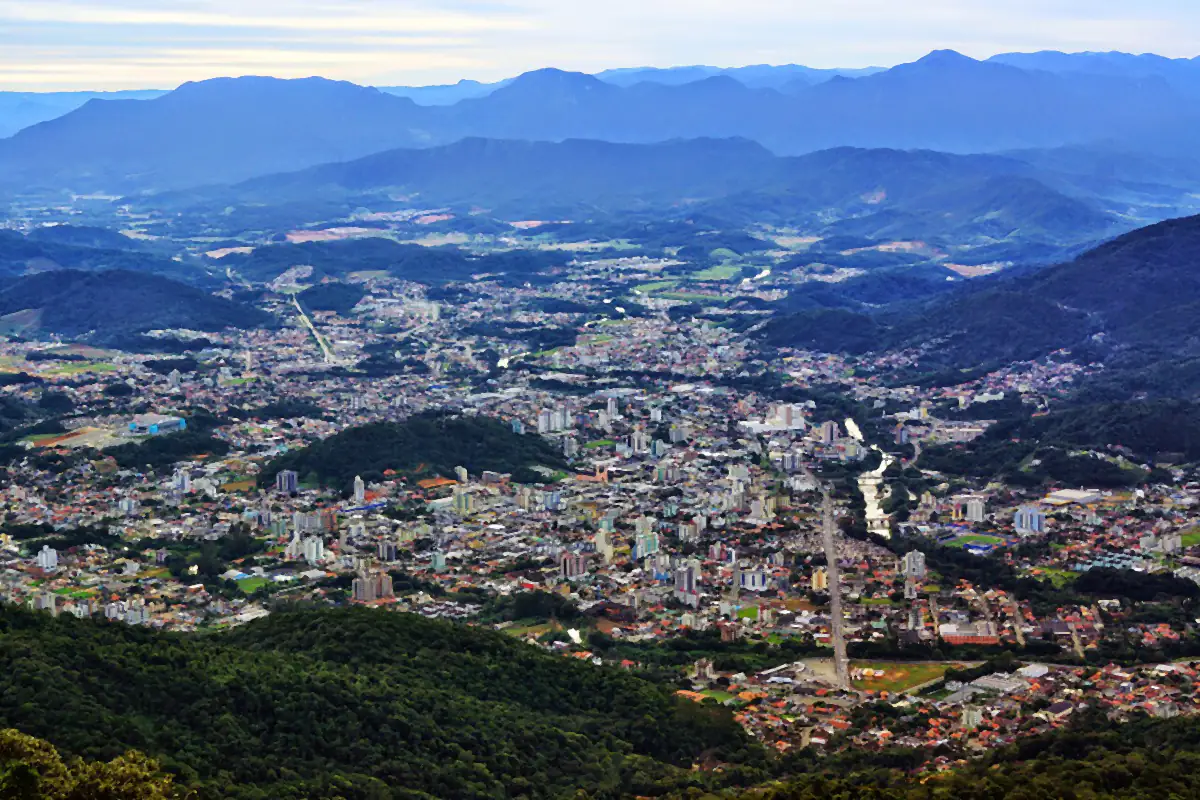 Vista aérea de Jaraguá do Sul a partir do Morro da Antena, com a cidade no vale e cadeias de morros azuladas ao fundo
