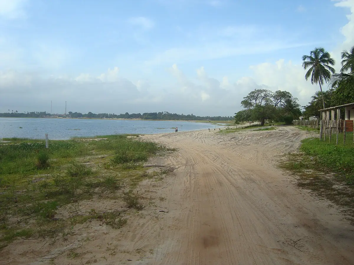 Lagoa de Jijoca, em Jijoca de Jericoacoara, com estrada de areia, coqueiros e céu azul com nuvens