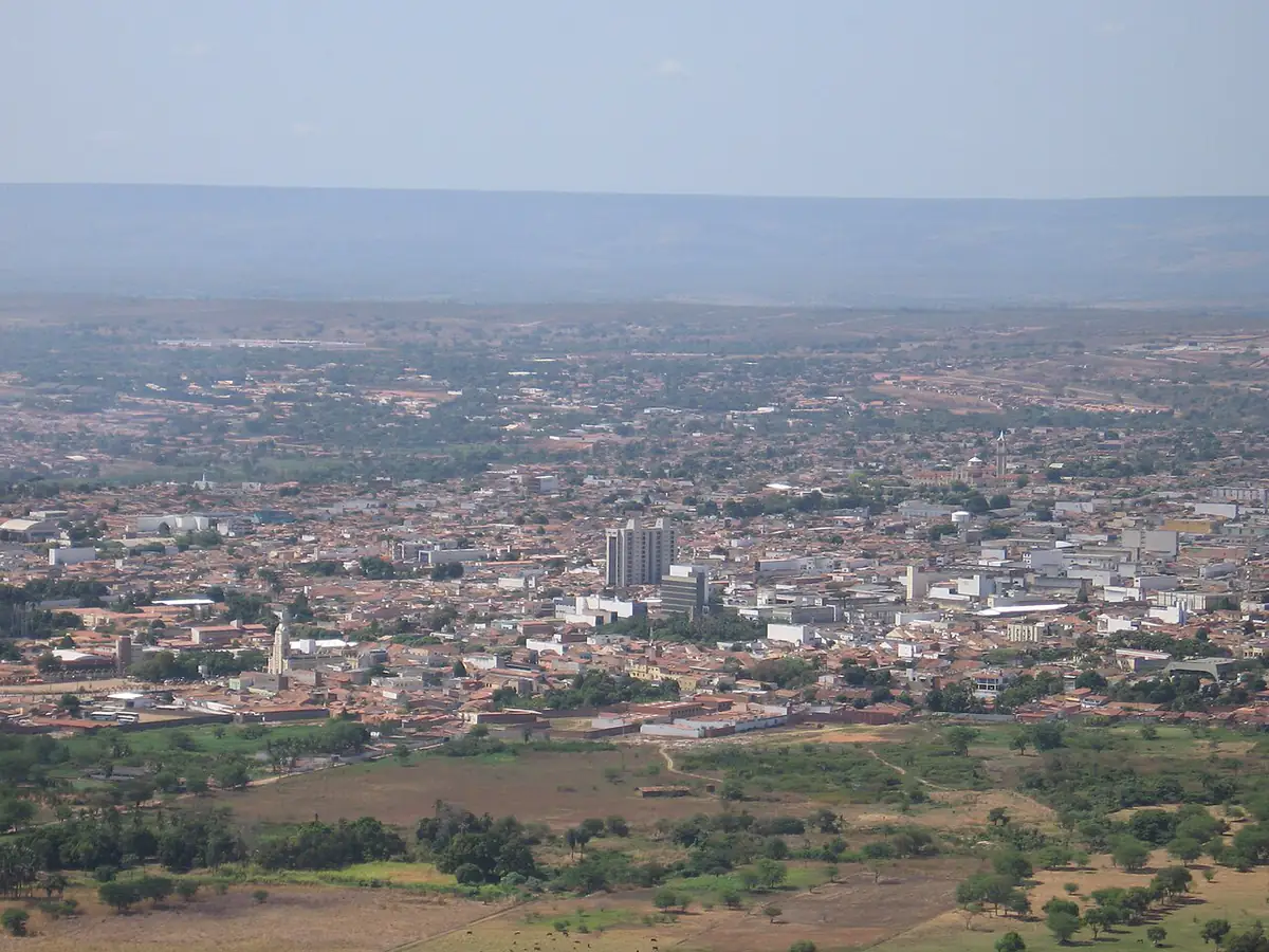 Vista aérea de Juazeiro do Norte a partir do Horto, com prédios e telhados e a Chapada ao fundo sob céu claro