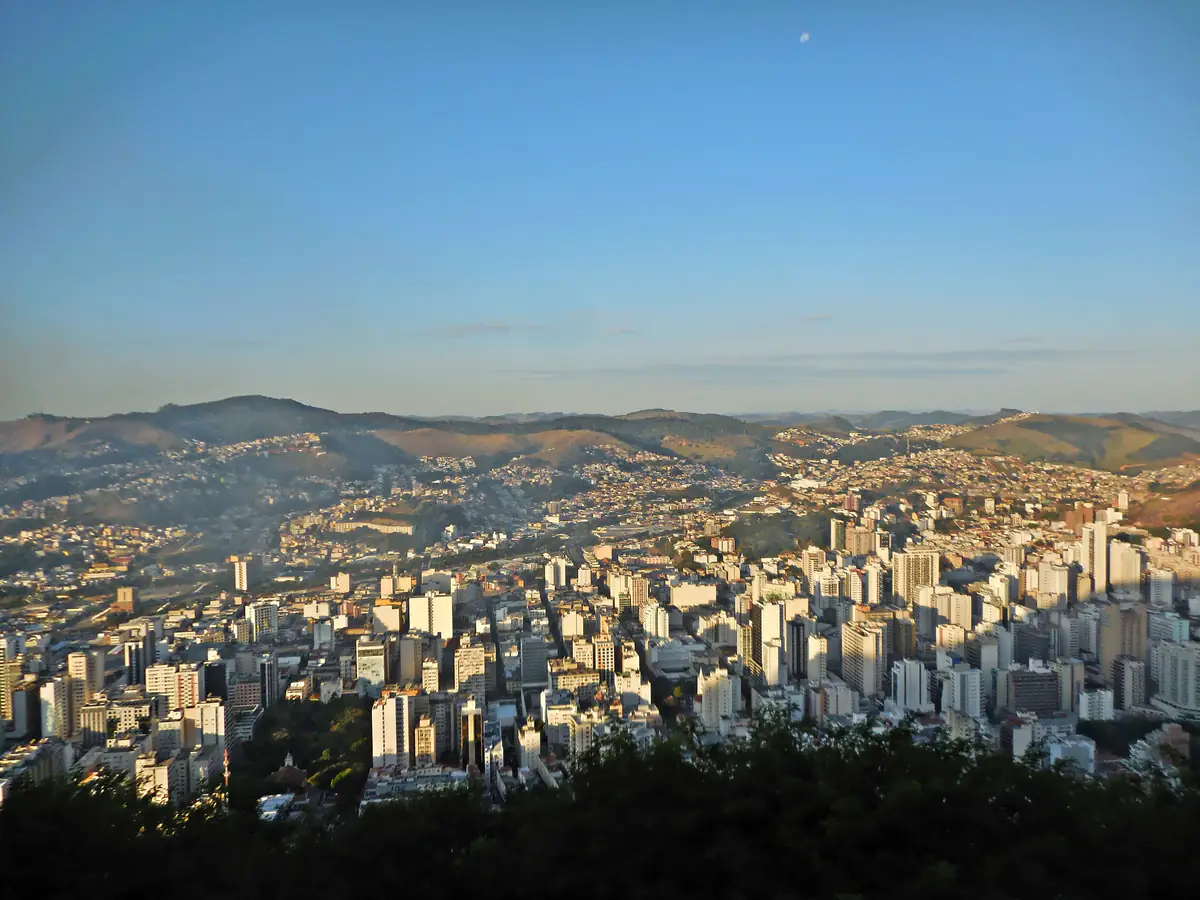 Vista aérea de Juiz de Fora a partir do Morro do Imperador, com prédios do centro entre colinas ao entardecer