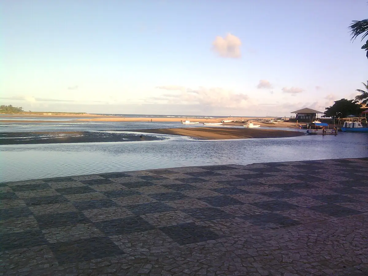Foz de rio na praia de Buraquinho, em Lauro de Freitas, com barcos e céu com poucas nuvens
