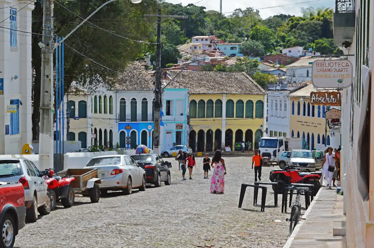Rua de pedra no centro histórico de Lençóis, com casarões coloridos e morros verdes ao fundo sob céu parcialmente nublado
