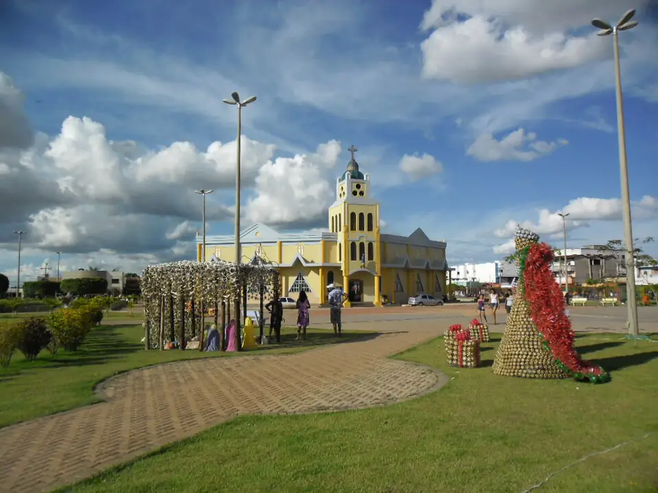 Praça com a igreja amarela de Luís Eduardo Magalhães sob céu azul com nuvens carregadas