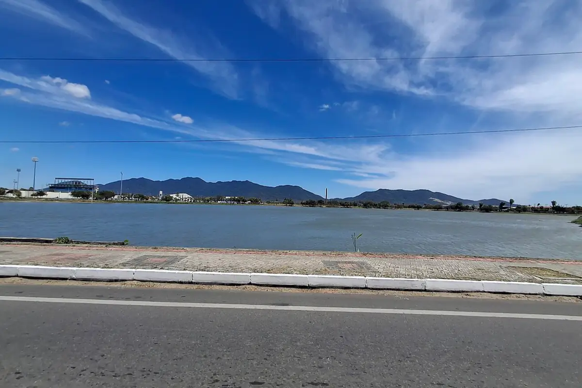 Lagoa de Maracanaú sob céu azul com nuvens finas, com serras ao fundo