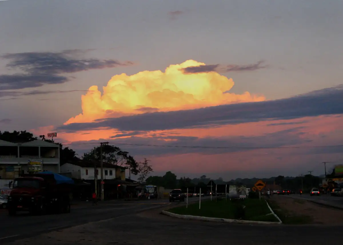 Nuvem iluminada de amarelo pelo pôr do sol sobre uma rodovia com carros e casas, em Marituba