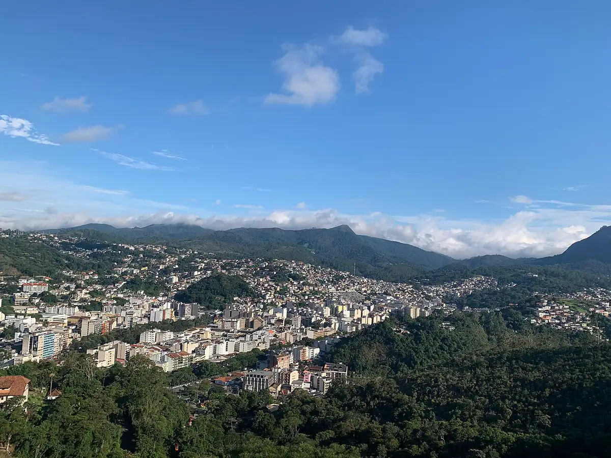 Vista aérea de Nova Friburgo com prédios no vale, montanhas cobertas de mata e nuvens baixas ao fundo