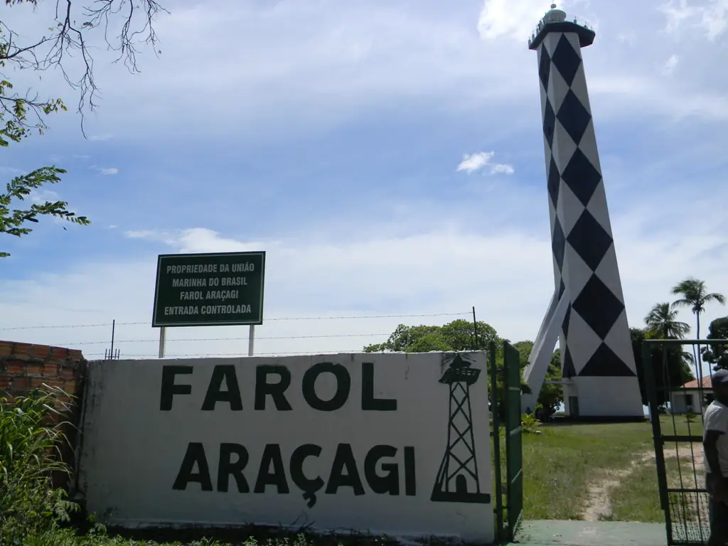 Farol Araçagi, torre listrada em losangos pretos e brancos, com céu azul e nuvens