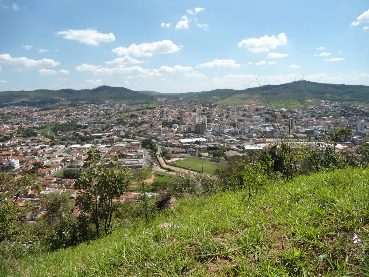 Vista parcial de Pará de Minas a partir de um morro, cidade cercada por colinas sob céu azul com nuvens
