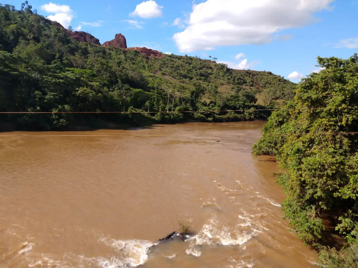 Rio Parauapebas com água barrenta, mata nas margens e um morro de terra vermelha ao fundo