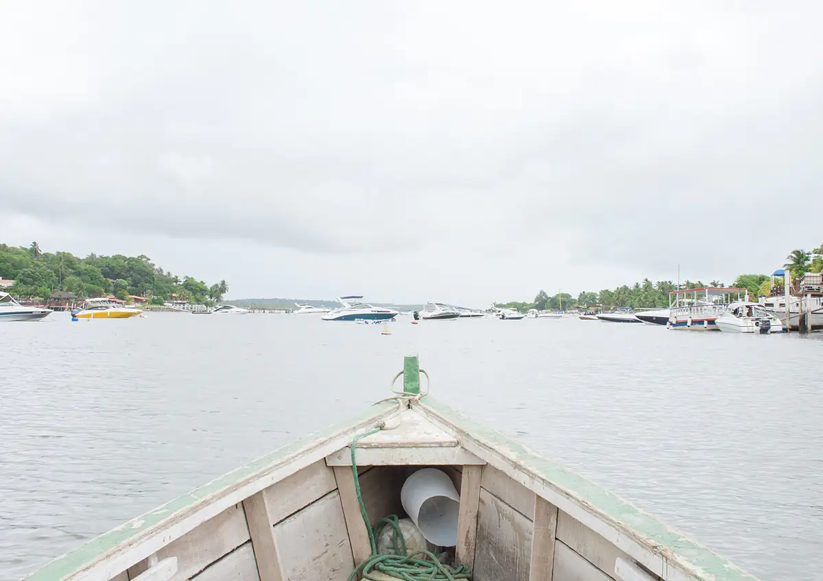 Proa de um barco no estuário de Maria Farinha, em Paulista, com lanchas ao fundo e céu nublado