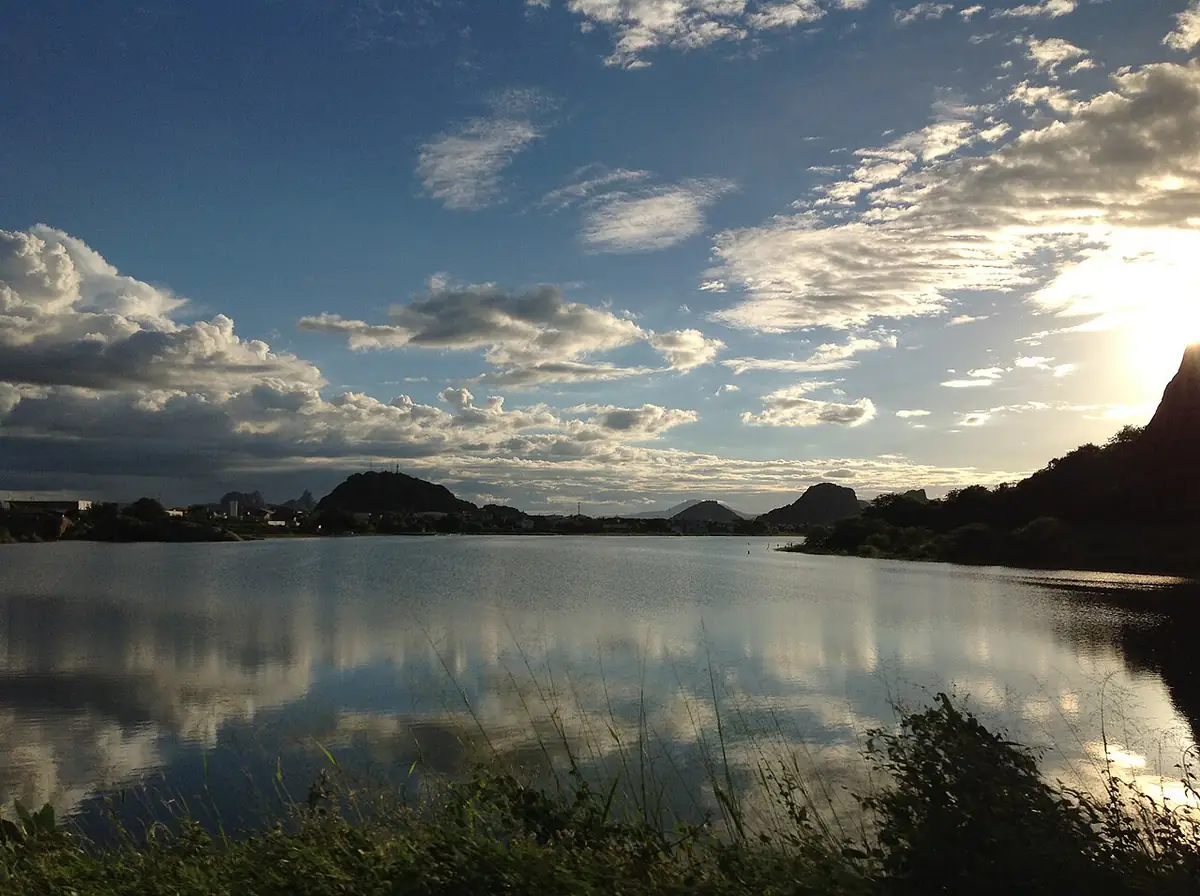 Açude com monólitos de pedra ao fundo e céu com nuvens ao entardecer, em Quixadá