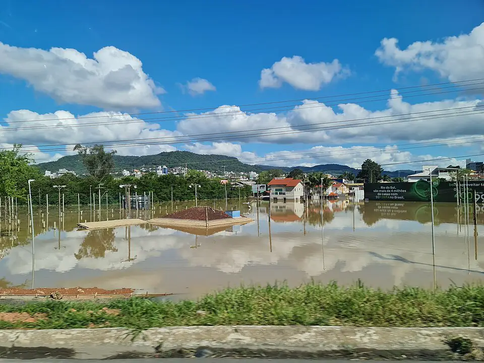Rua e casas alagadas de Rio do Sul durante a enchente de outubro de 2023, com morros ao fundo e céu azul com nuvens